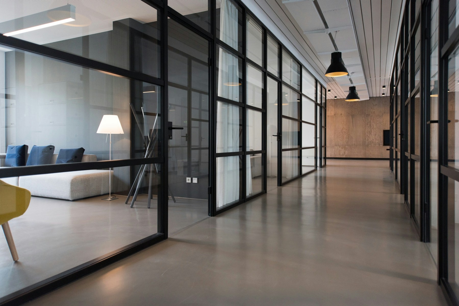 A bright, orderly office corridor with glass meeting rooms and polished floors